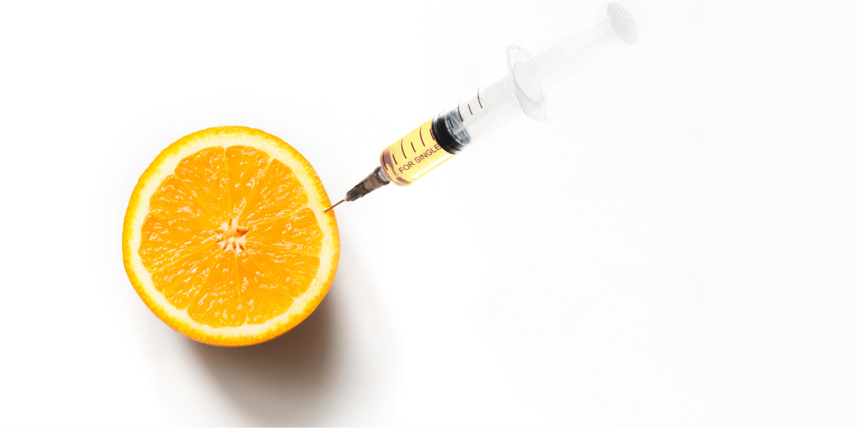 A syringe getting juice from a half orange