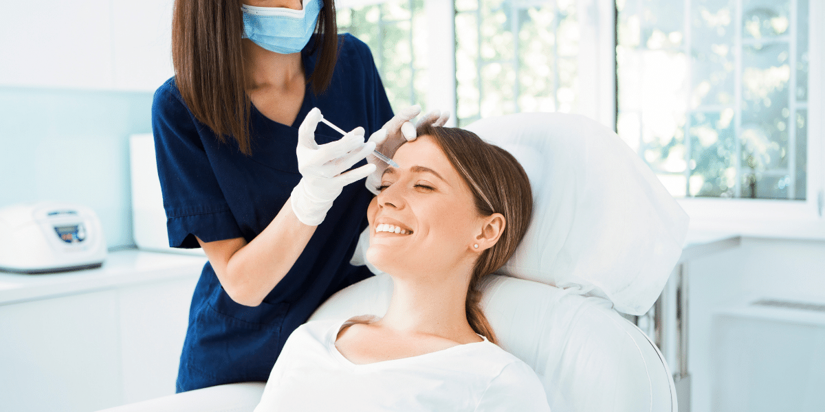 Female healthcare profession administering Botox in smiling lady's forehead