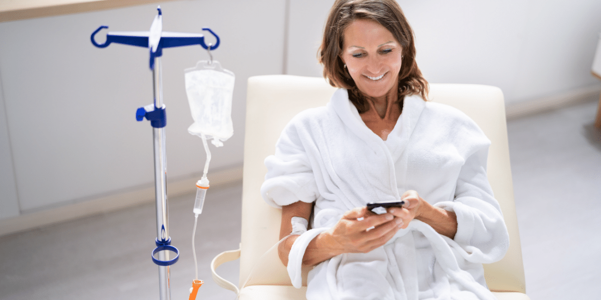 Lady smiling and playing on her phone while getting a drip.