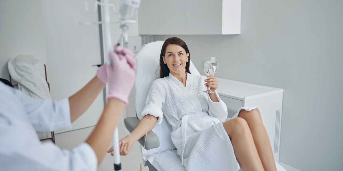 Nurse administering an IV drip to happy woman in robe and drinking water.