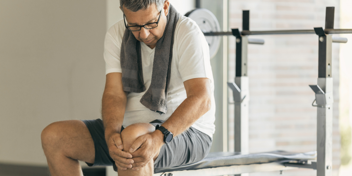 Older man sitting on a workout bench holding his injured knee